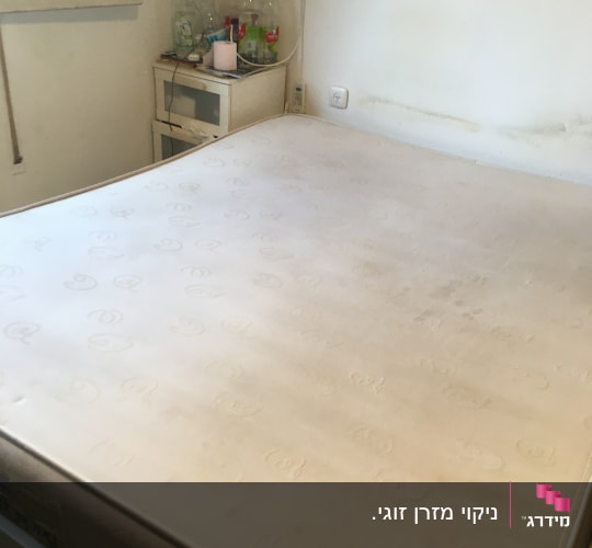 מזרן על מיטה עם כתמים קלים ליד שולחן קטן עם בקבוקים
